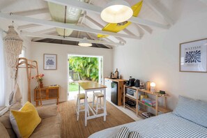 A cozy room with a bed, a dining table, a kitchen area, and a view of greenery outside.