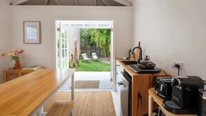 Una cocina con una mesa de madera, una cafetera y vistas a un patio trasero con valla de madera y sillas.