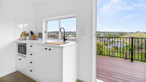 A modern kitchen with a large window, a wooden deck, and a view of a residential area. - Cute 1-Bed Tiny House with Garden in Nature (Bridgeman Downs)