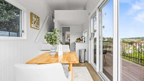 A modern kitchen with white cabinets, a wooden countertop, and a view of the outdoors. - Cute 1-Bed Tiny House with Garden in Nature (Bridgeman Downs)