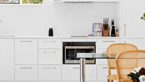 A modern kitchen with white cabinets, a dining table, and a wicker chair. - Chic 1-Bed Escape with Parking Bridgeman Downs (Bridgeman Downs)