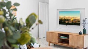 A modern living room with a television mounted on the wall, a wooden cabinet below, and a door to the left. - Chic 1-Bed Escape with Parking Bridgeman Downs (Bridgeman Downs)