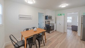 Une cuisine compacte équipée d’un four à micro-ondes, d’un four et de placards. On y trouve une table à manger avec des chaises et un petit réfrigérateur.