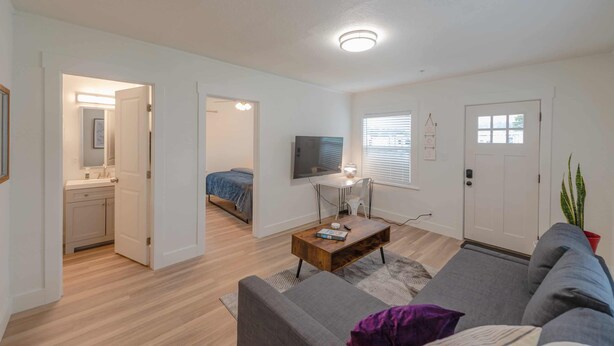 Un salon moderne avec un canapé, une table basse et un téléviseur. Une porte donne accès à une chambre et à une salle de bain.