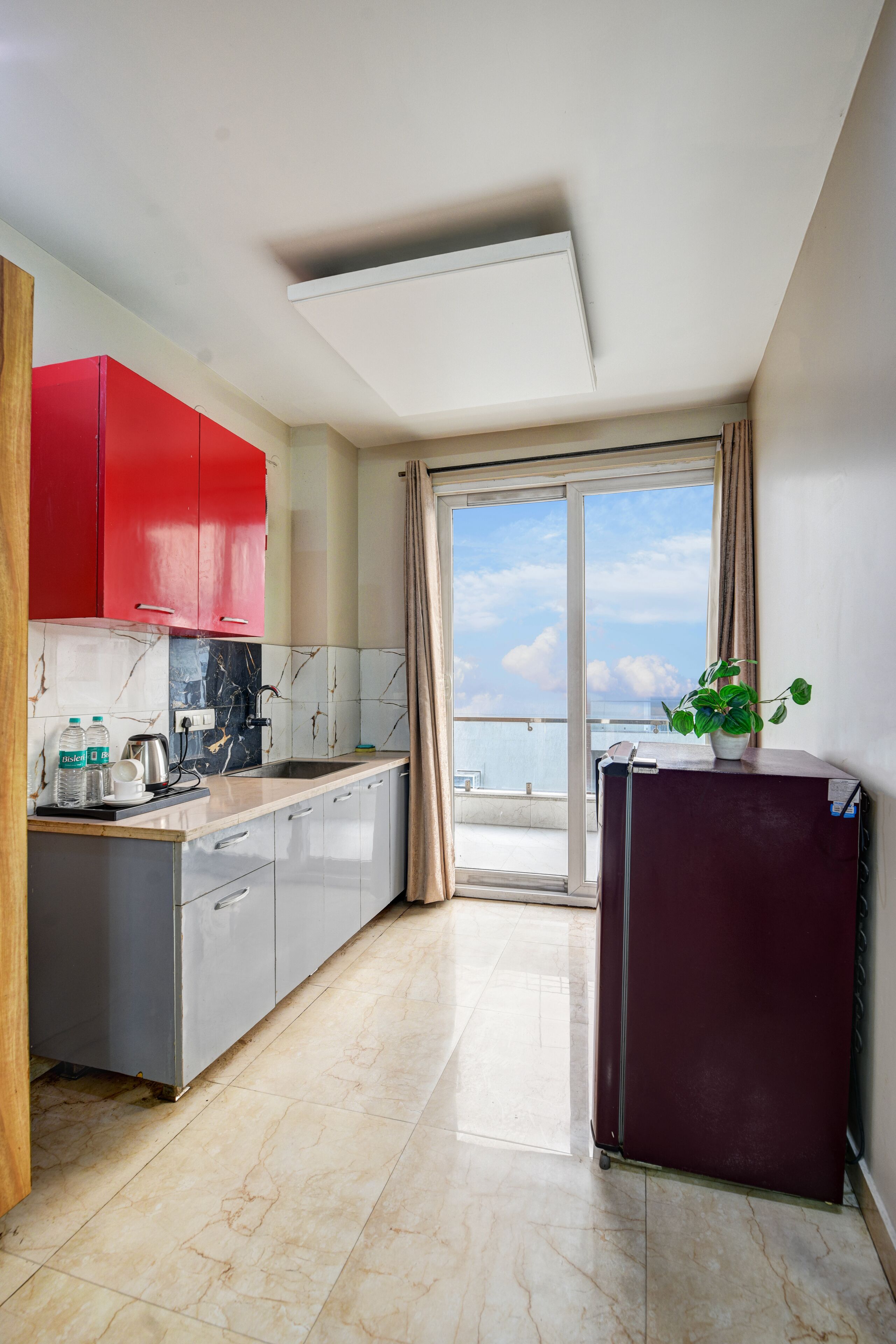 Una cucina moderna con mobili rossi, zoccolo in marmo e vista sul mare tramite una porta scorrevole in vetro.