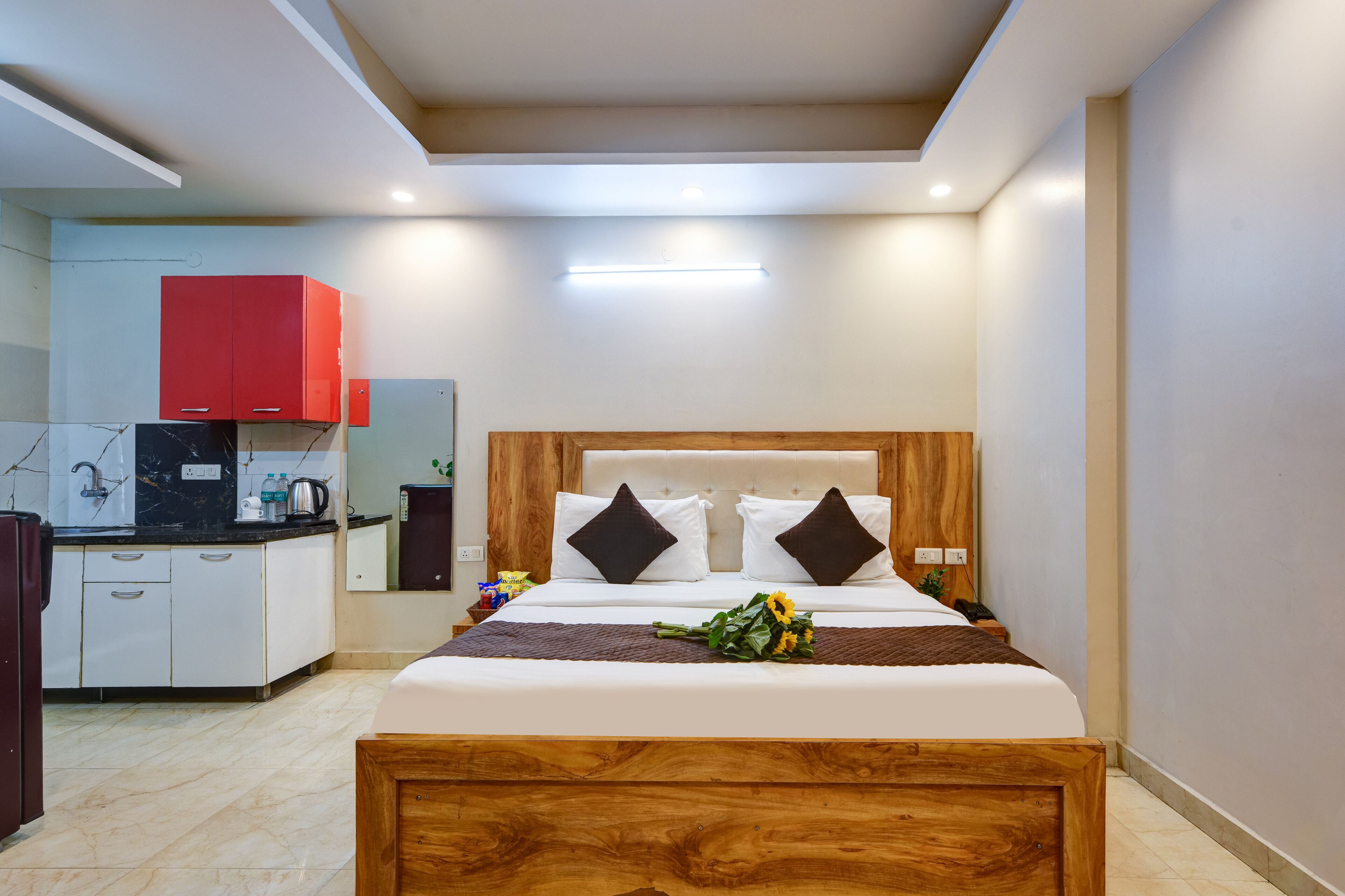 Una habitación de hotel con una cama de madera, ropa de cama blanca, un armario rojo y una kitchenette.