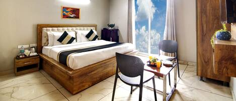 A hotel room with a bed, a desk with a chair, a wardrobe, and a large window with a view of the sky.