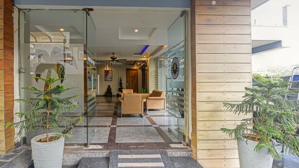 A hotel lobby with a glass entrance, a reception desk, and a seating area. - The Palm Suites (Gurugram)