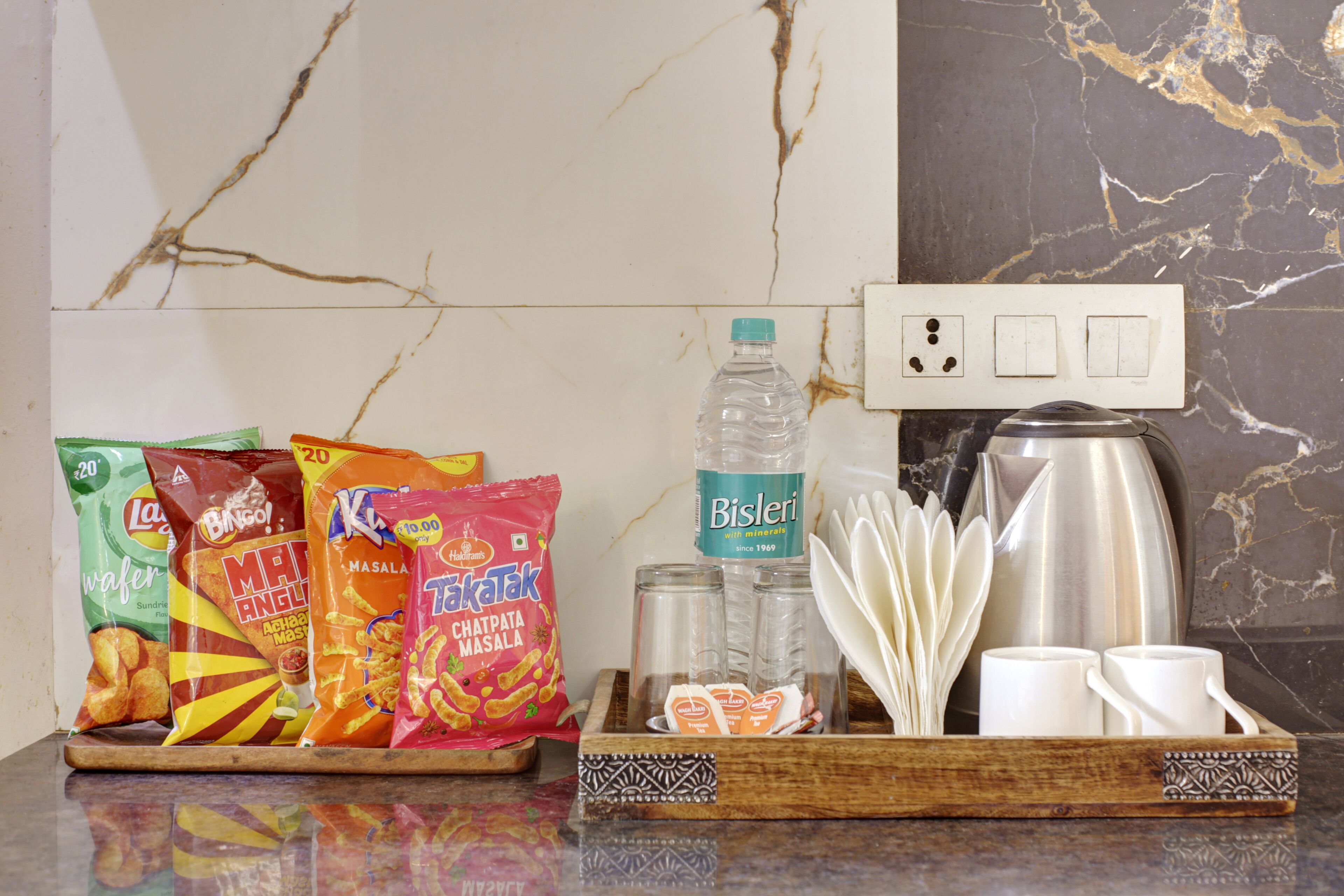 A tray with snacks, a water bottle, salt and pepper shakers, a coffee pot, and white cups on a marble countertop.