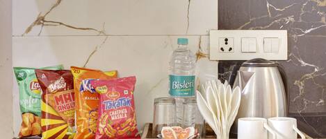 A tray with snacks, a water bottle, salt and pepper shakers, a coffee pot, and white cups on a marble countertop.