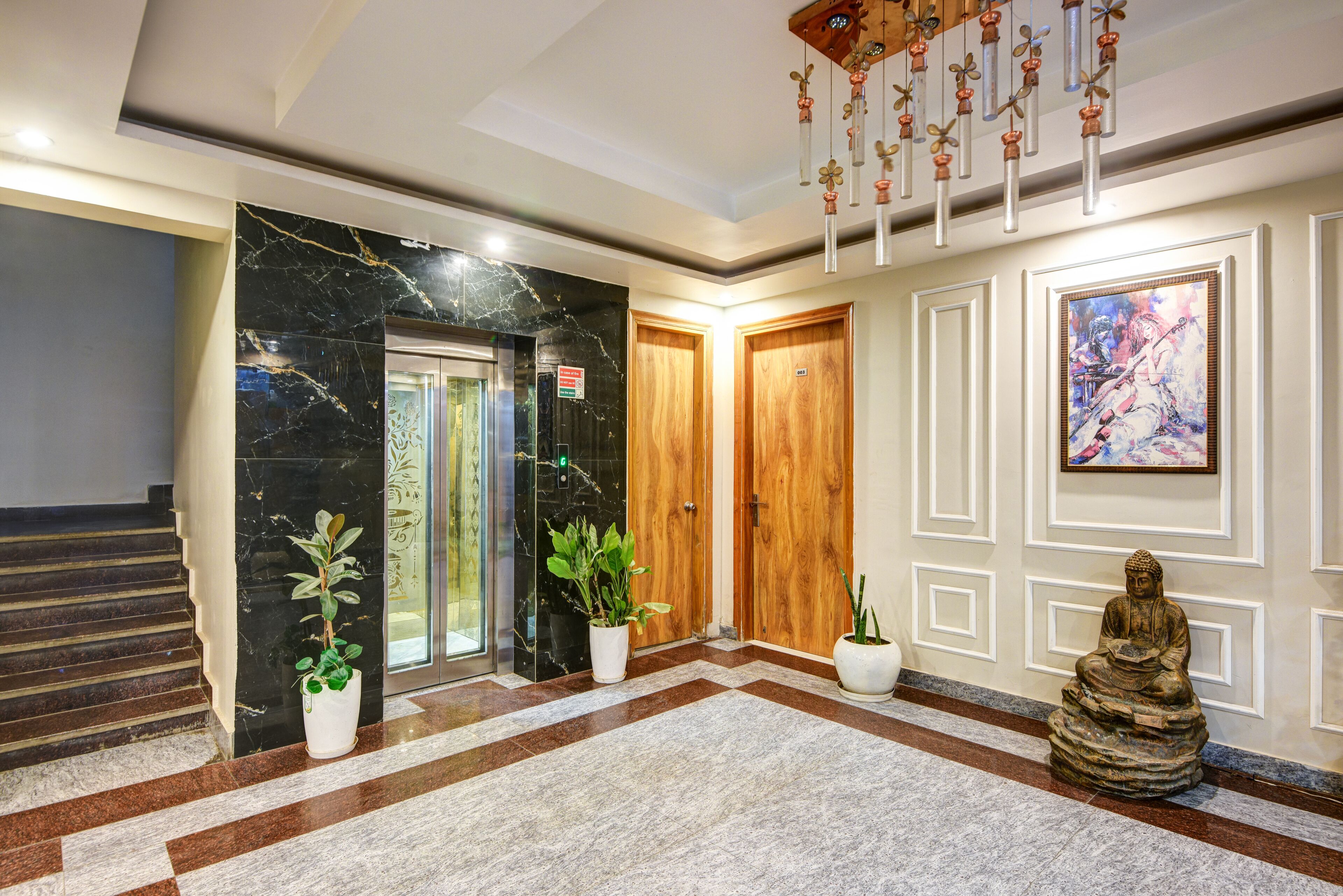 Un vestíbulo con piso de mármol, puertas de madera, plantas en macetas y una estatua de Buda.