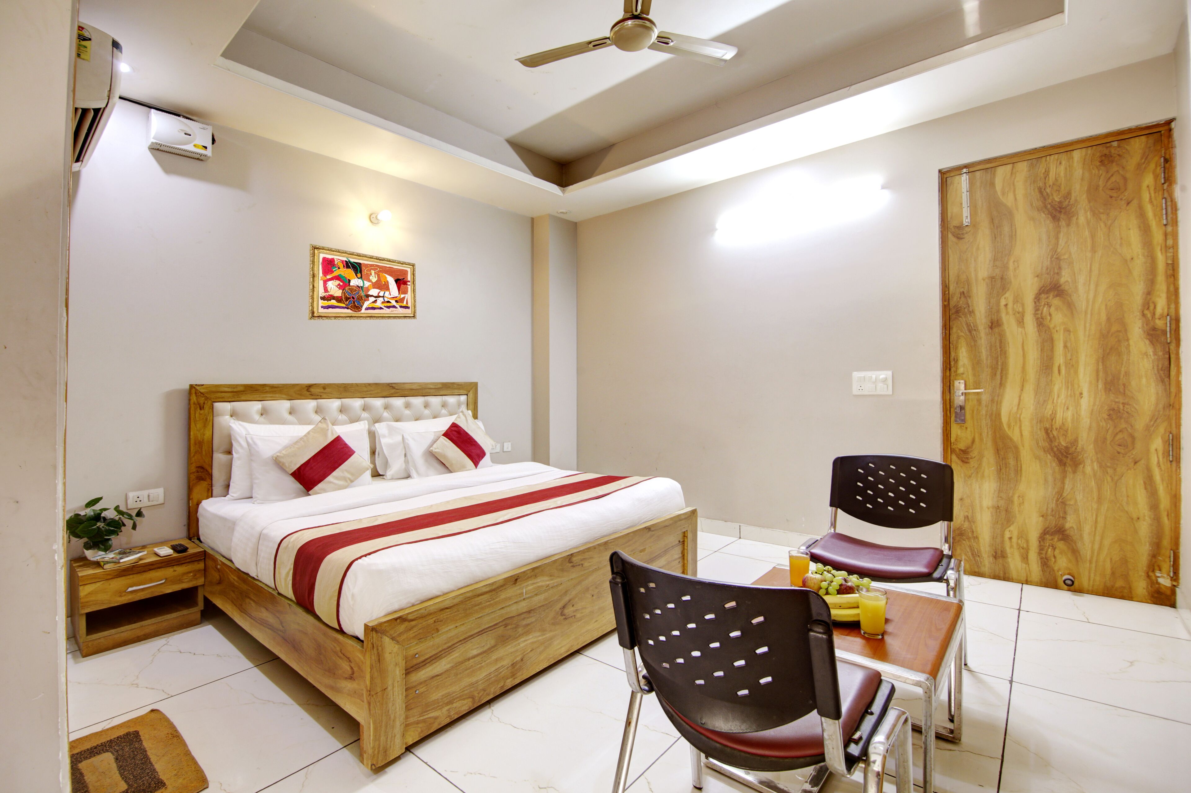 A bedroom with a wooden bed, a bedside table, a chair, and a small table with fruit and a glass of juice.