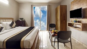 A hotel room with a bed, a desk with a chair, a TV mounted on the wall, and a window with a view of the sky. - The Palm Suites (Gurugram)
