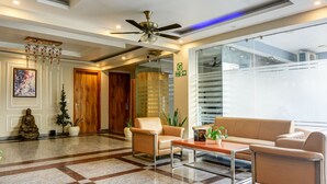 A lobby with a checkered floor, a ceiling fan, a reception desk, and a large window. - The Palm Suites (Gurugram)