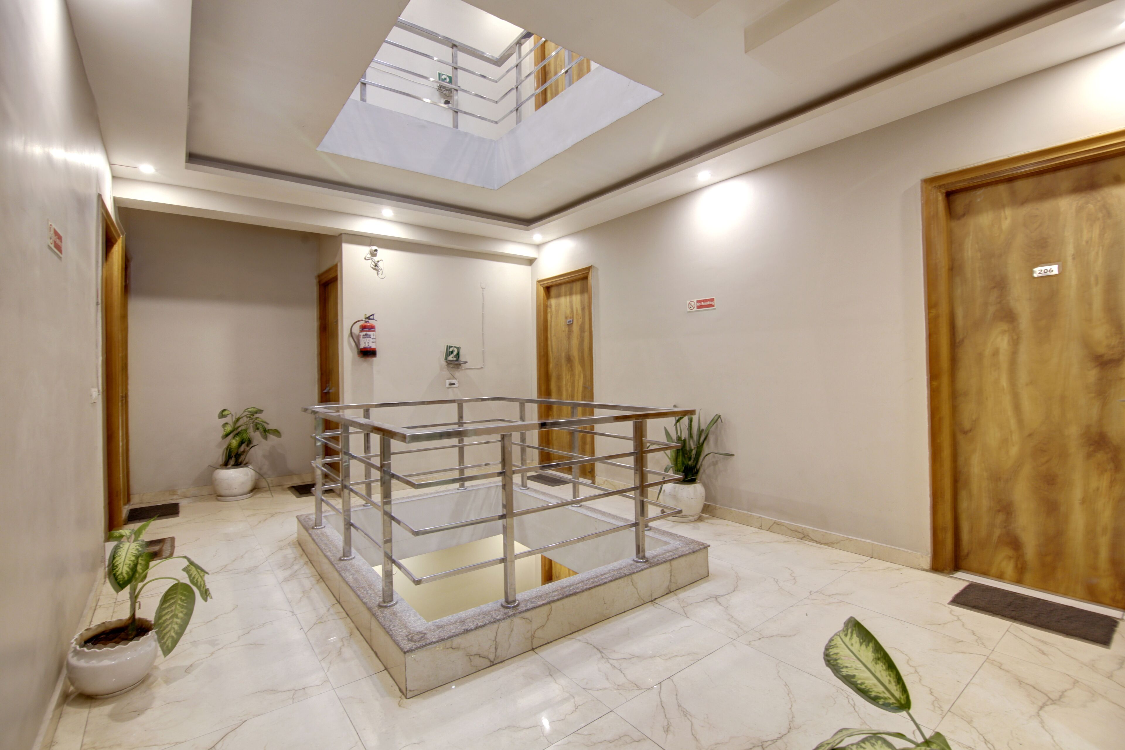 Um hall de hotel com guarda-corpo de vidro, plantas em vasos, piso de mármore e portas de madeira.
