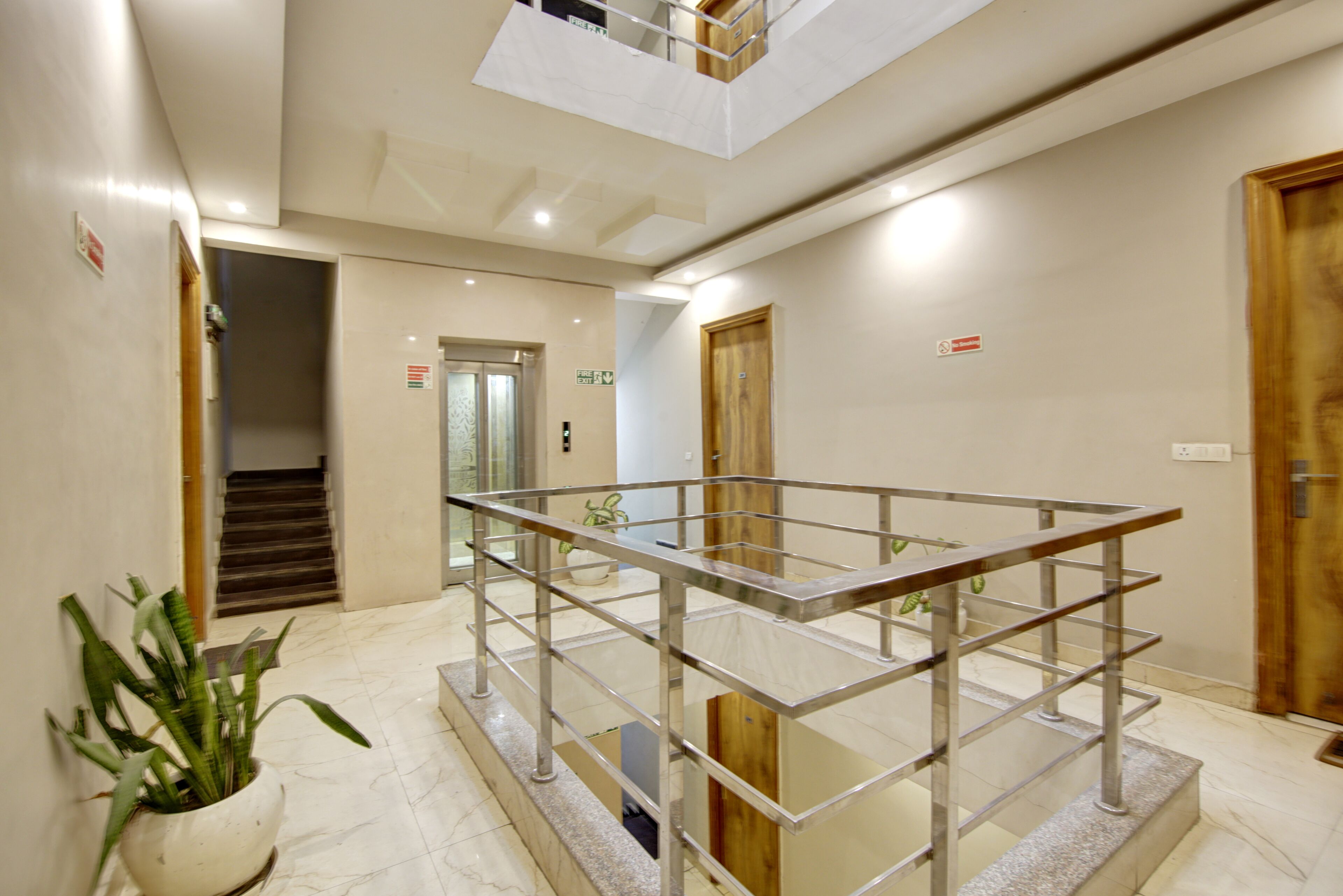 A modern hotel lobby with a glass railing, a potted plant, and a staircase.