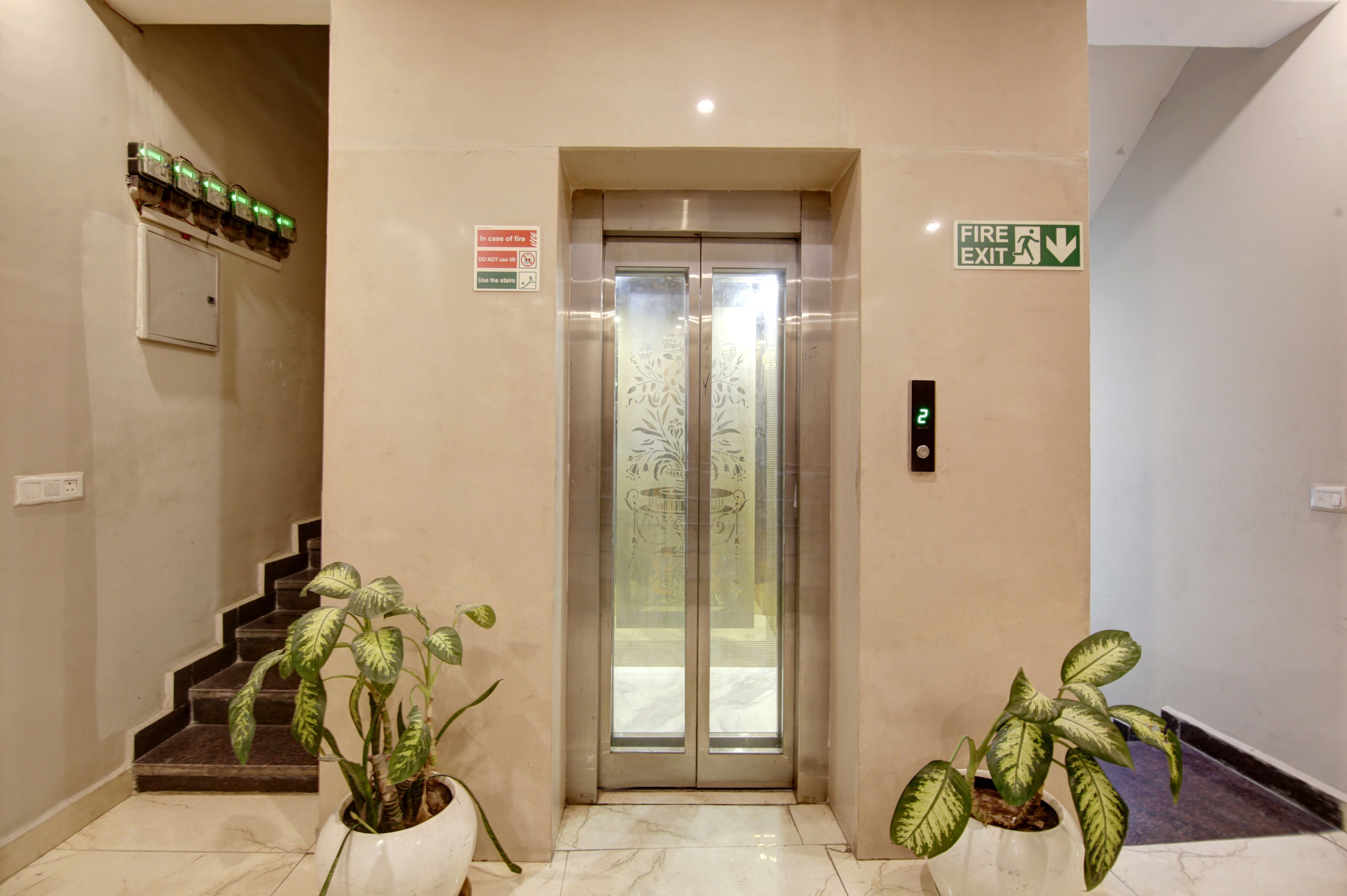 An elevator with a fire exit sign, a staircase, and potted plants.