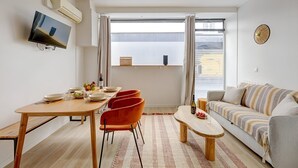 En moderne stue med spiseplads, sofa og et fjernsyn ophængt på væggen.