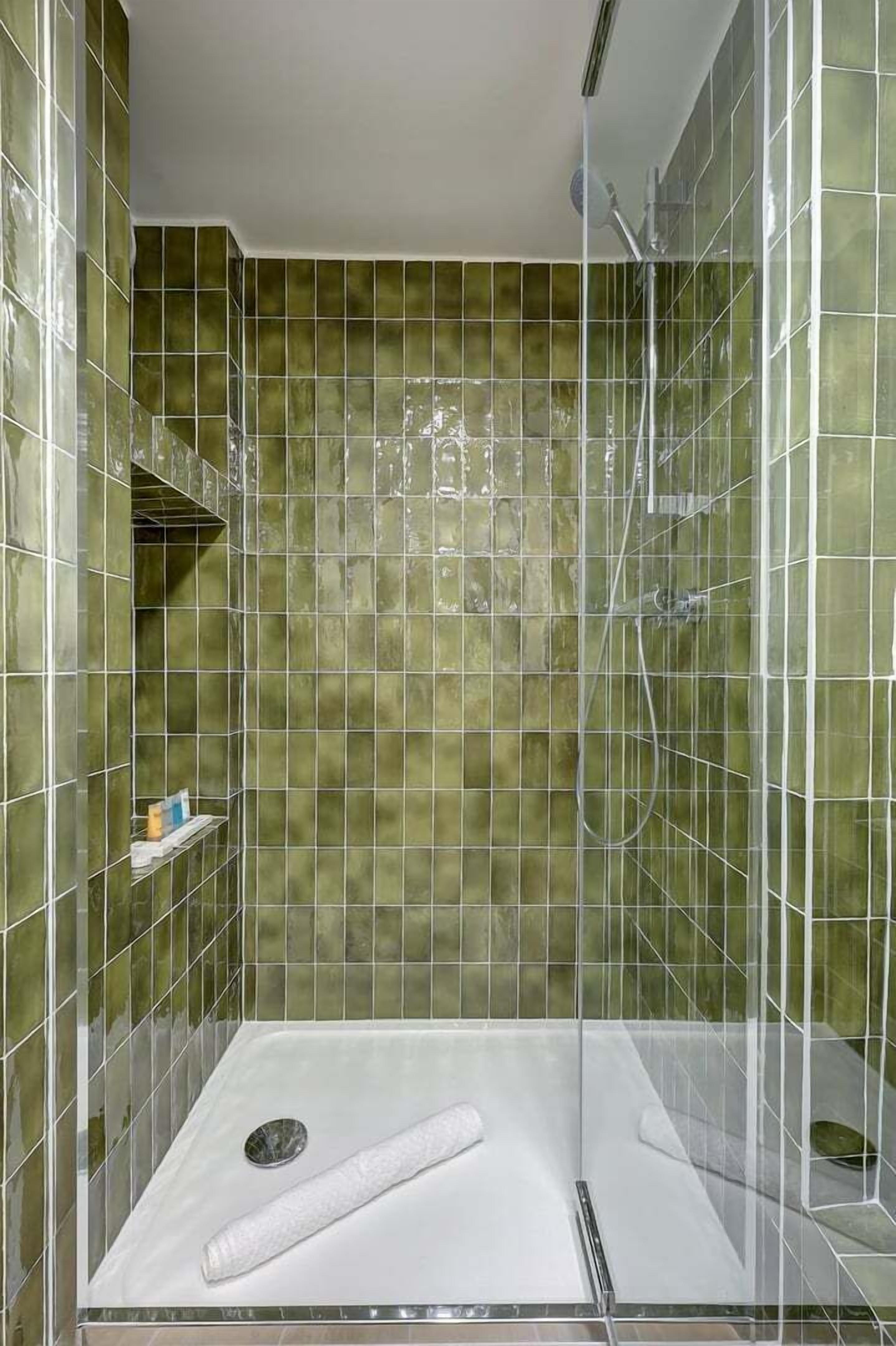 Une douche avec une paroi en verre et des murs recouverts de carreaux verts.