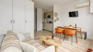 En moderne stue med sofa, sofabord i træ og et spiseområde med to stole og et bord.