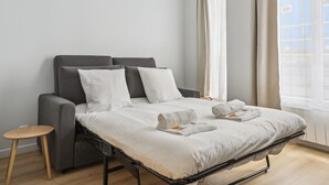 Habitación de hotel moderna con cama, cabecera gris, almohadas blancas y una mesita de madera.