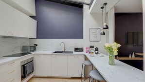 A modern kitchen with white cabinets, a black countertop, a built-in oven, a microwave, a sink, and a bar area with stools. - TBS 151- Lovely suite near Place de la République (Paris)