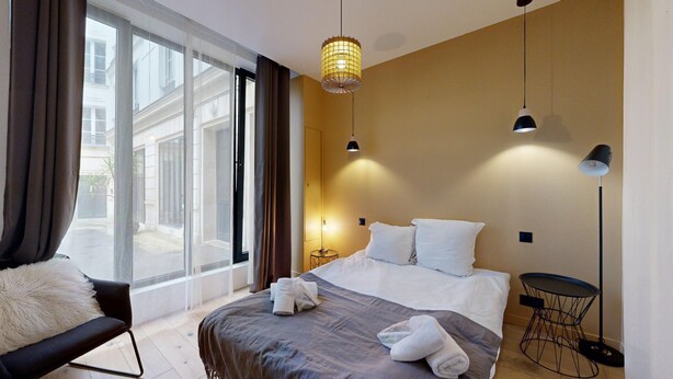 A modern hotel room with a large bed, a chair, a small table, and a view of the outside. - TBS 151- Lovely suite near Place de la République (Paris)