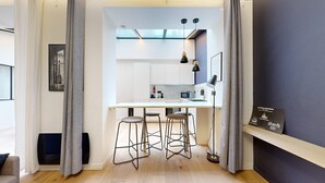 A compact kitchen with a white countertop, two stools, and modern pendant lighting. - TBS 151- Lovely suite near Place de la République (Paris)