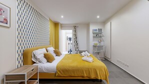 A hotel room with a bed, a yellow bedspread, a wooden side table, a mirror, and a shower area. - TBS 6 - Beautiful apartment near Opéra Garnier (Paris)