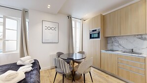 A compact hotel room with a bed, a round dining table with chairs, a kitchenette, and a large window with curtains. - TheBlueStay 27 - Charming and elegant studio (Paris)
