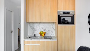 A compact kitchen with wooden cabinets, a marble backsplash, a sink, and a built-in oven.