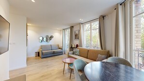 A modern living room with a grey sofa, a round table, and a balcony with a view of the city.