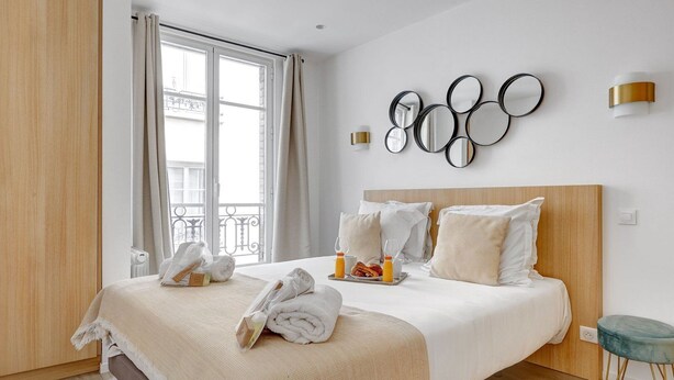 A hotel room with a large bed, a wooden headboard, a wall-mounted mirror, and a view of the outside balcony. - TheBlueStay 31 – Modern Apartment – Paris 13 (Paris)