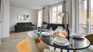 A modern living room with a dining area, a grey sofa, and a dining table set for a meal. - Bluestay 33 - Charming apartment in Paris (Paris)