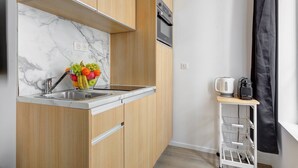 A compact kitchen with a marble backsplash, wooden cabinets, a stainless steel sink, and a fruit bowl on the counter. - TBS 34 - Elegantly designed apartment (Paris)