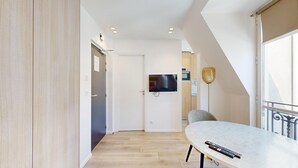 Un salon moderne avec un téléviseur à écran plat fixé au mur, une table ronde sur laquelle sont posées des télécommandes et un fauteuil.