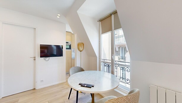 Un salon moderne avec une table ronde, un téléviseur fixé au mur et un balcon offrant une vue sur la ville.