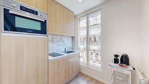 Une cuisine moderne dotée d’un four encastré, d’un pare-feu en marbre et d’une fenêtre donnant sur un balcon.