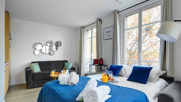 A hotel room with a large bed, a sofa, a coffee table, and a wall-mounted mirror. - TBS 35 - Cosy and refined apartment (Paris)