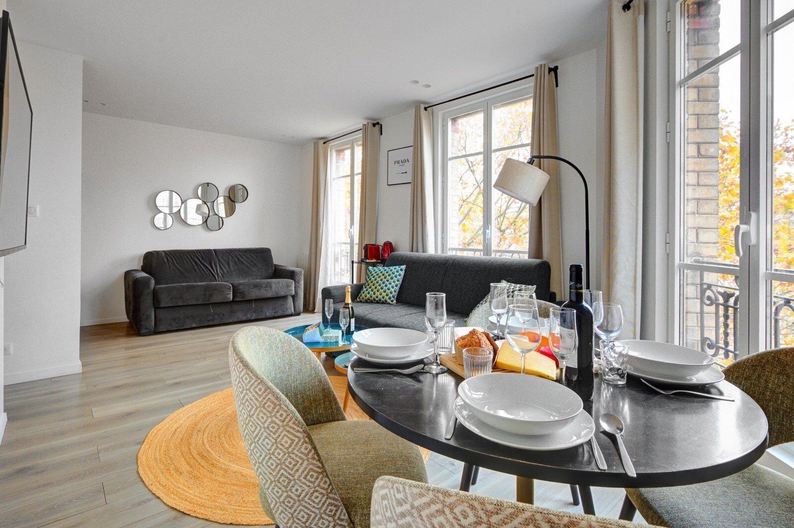 A modern living room with a dining area, a grey sofa, and a dining table set for a meal.