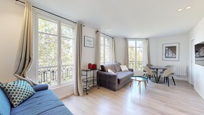 A spacious living area with a sofa, a small round table, and a balcony with a railing. - TBS 35 - Cosy and refined apartment (Paris)