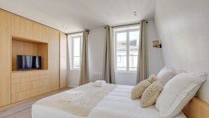 A hotel room with a bed, a TV mounted on a wooden panel, and a window with curtains. - TBS 38 - Cosy and elegant duplex apartment (Paris)