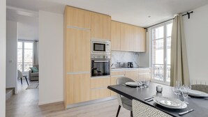A modern kitchen with wooden cabinets, a built-in oven, and a dining area with a table set for four. - TBS 38 - Cosy and elegant duplex apartment (Paris)