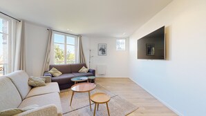 A modern living room with a sofa, two small tables, a large TV, and a radiator. - TBS 38 - Cosy and elegant duplex apartment (Paris)