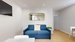 A modern living room with a blue sofa, a white armchair, and a small side table with a plant. - TBS 196 - Charming apartment in the Marais (Paris)