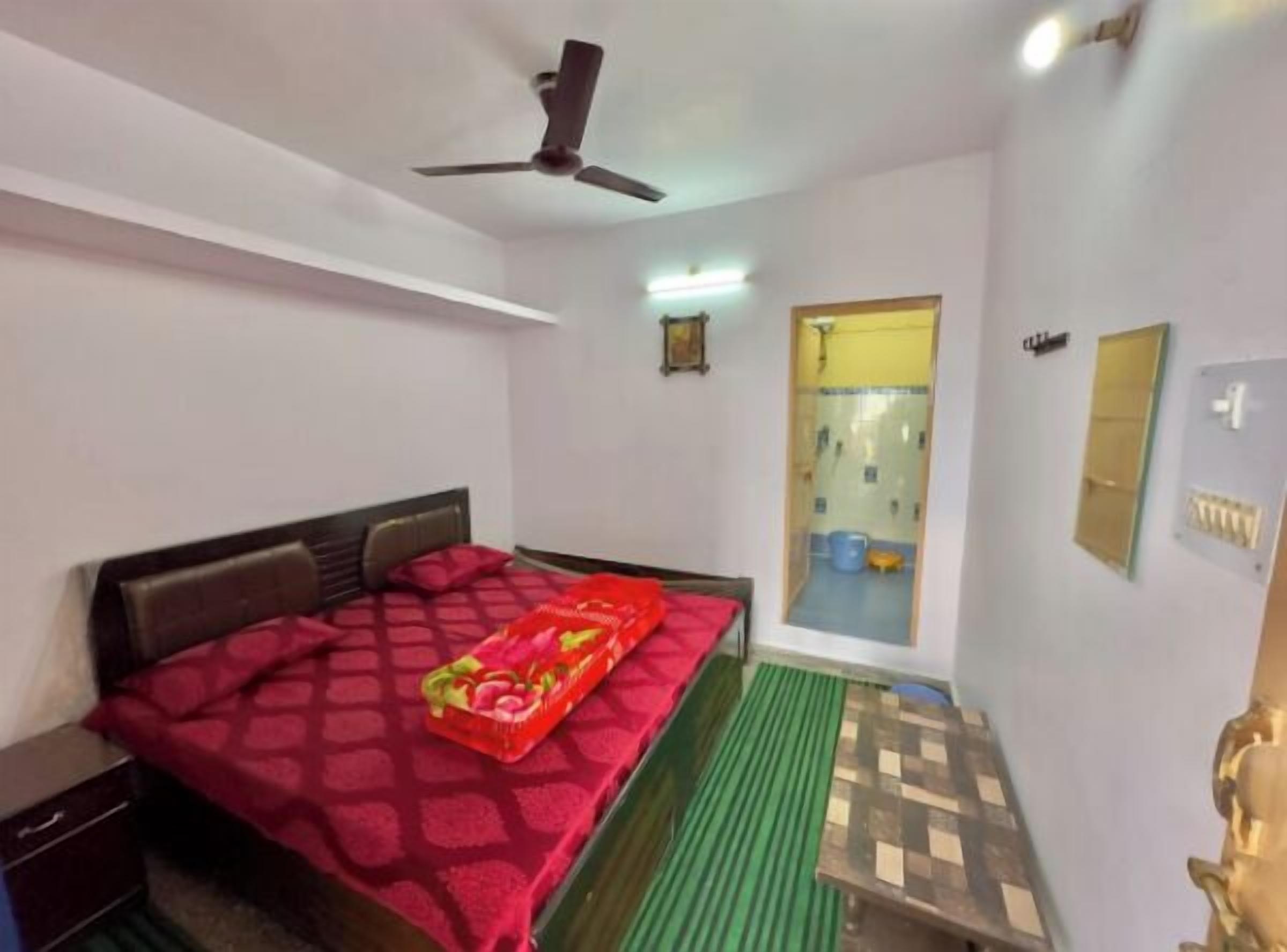 Une chambre à coucher comprenant un lit, une table de chevet, un ventilateur de plafond, une fenêtre et une porte donnant sur une salle de bain.