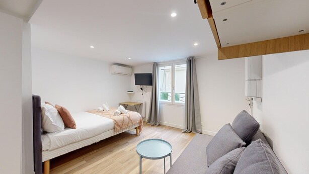 Ein modernes Schlafzimmer mit Bett, Nachttisch, Sofa und einem Fenster mit Vorhängen.