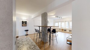 Een moderne woonkamer met een hoge plafond, een centrale pilaar en een eethoek met barstoelen.