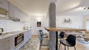 Een moderne keuken met grijze kastjes, een wit aanrechtblad en een inbouwoven. Er is een eethoek met een houten tafel en vier stoelen. Op de muur zit een sticker van een fiets, en een poster met de tekst 'Time is precious'.
