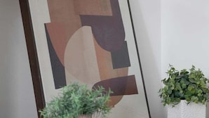 A framed abstract painting leaning against a wall, a small potted plant on a wooden dresser, and a white textured planter with green foliage.